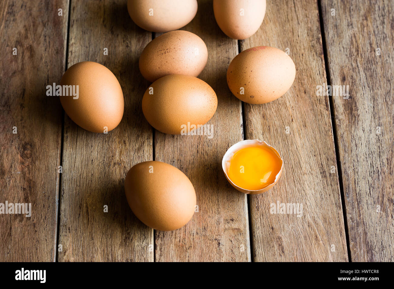 Fresco uova organiche sparse su legno tavolo da cucina, incrinature del guscio aperto con tuorlo, soft diurna, cottura, concetto di Pasqua, vista dall'alto Foto Stock