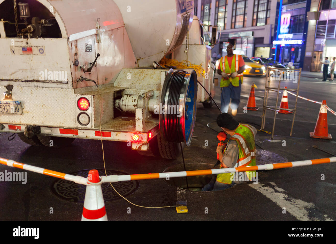 La città di New York, Stati Uniti d'America - Luglio 12, 2015: operai al lavoro in un tombino in Manhattan di notte. La grande città necessita di frequenti interventi di manutenzione. Foto Stock