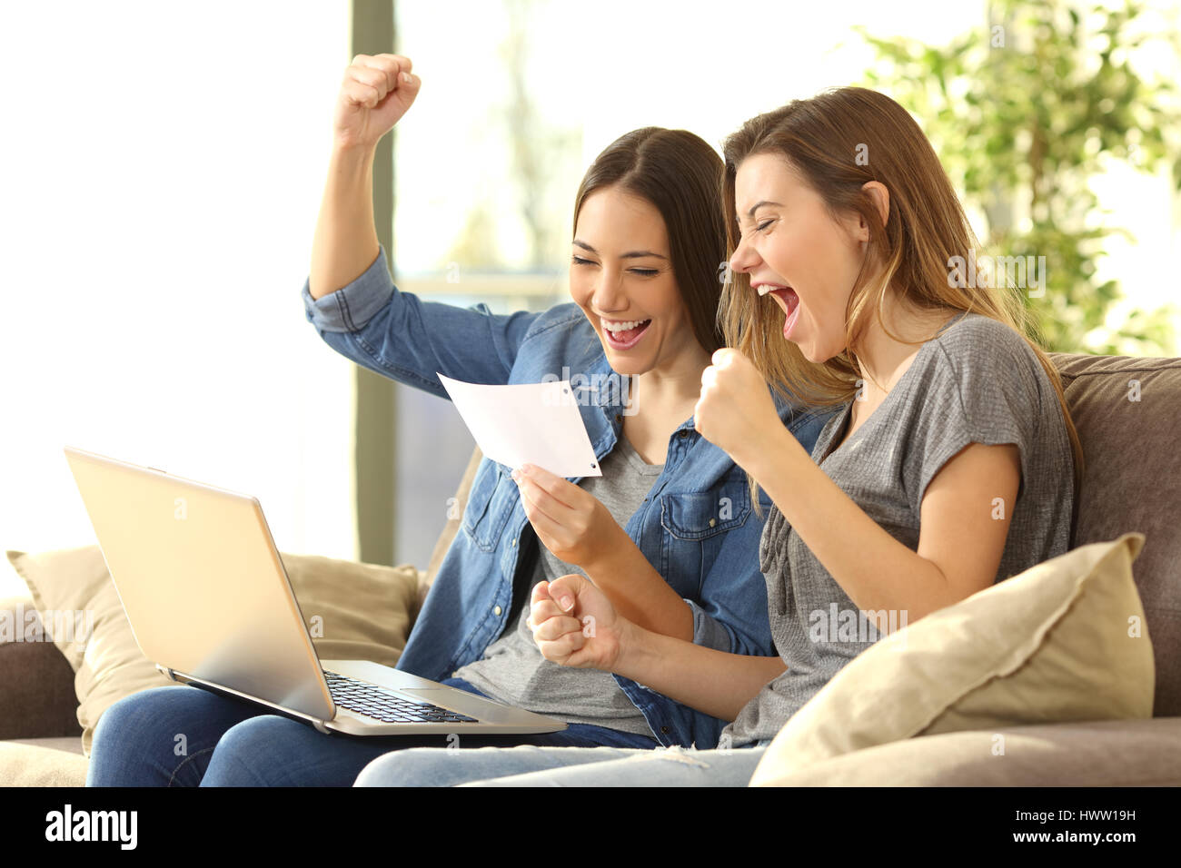 Emozionato coinquilini la lettura di una notifica della banca seduta su un divano nel soggiorno di casa Foto Stock