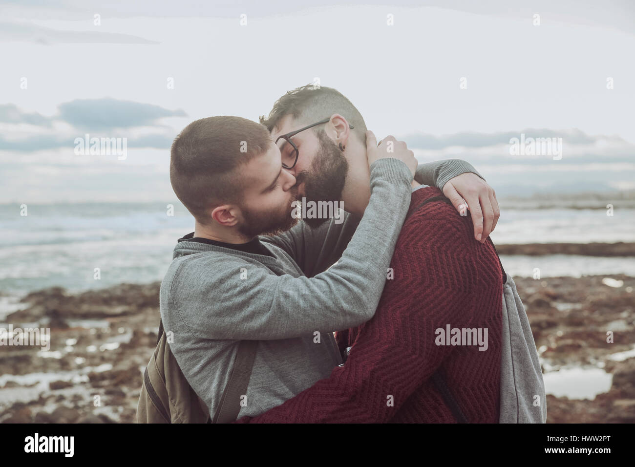 Giovane coppia gay abbracciando e baciando davanti al mare Foto Stock