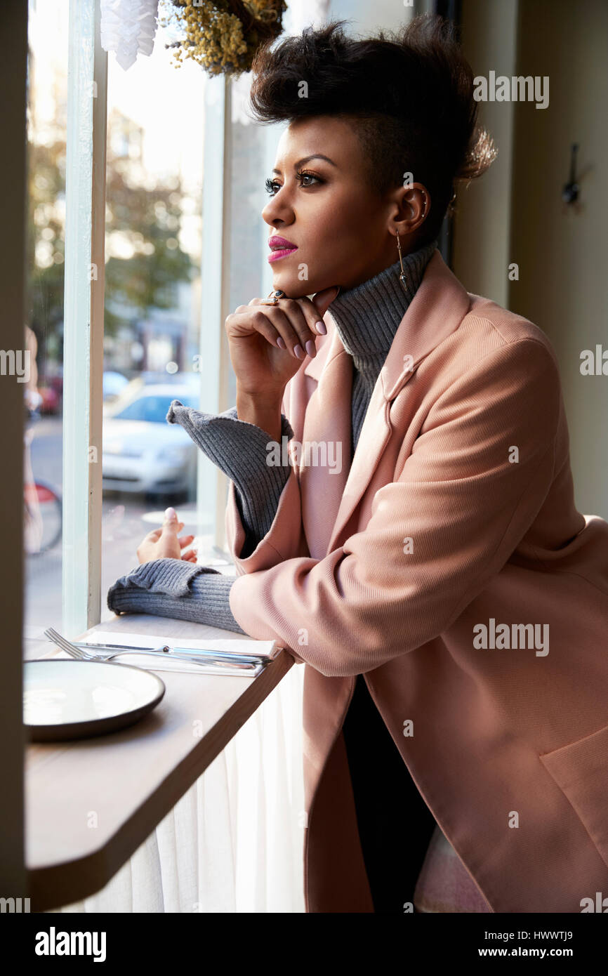 Elegante giovane donna in guardando fuori della finestra cafe, vista laterale Foto Stock