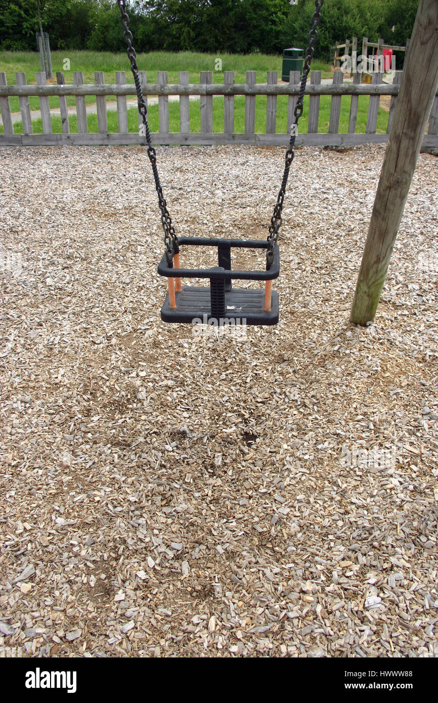 Park swing per un giovane bambino dove la corteccia scheggiata è lontano da indossare sotto. Recinzione, inferriata, erba e alberi in background. Foto Stock