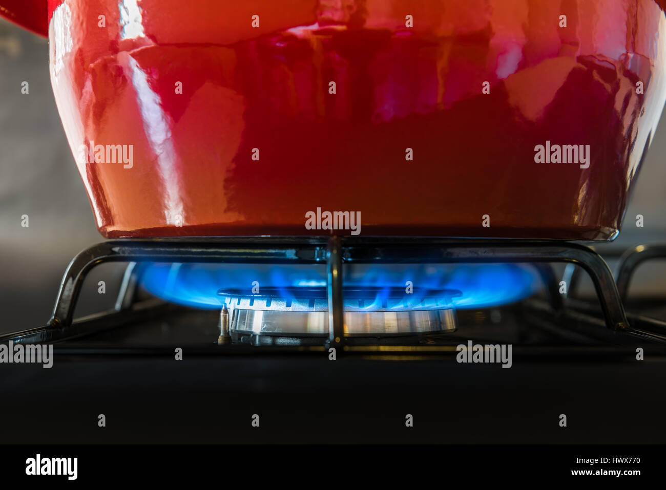 Un rosso brillante POT si siede sulla parte superiore del piano di cottura a gas di blue flames cuocere lentamente il contenuto. Foto Stock