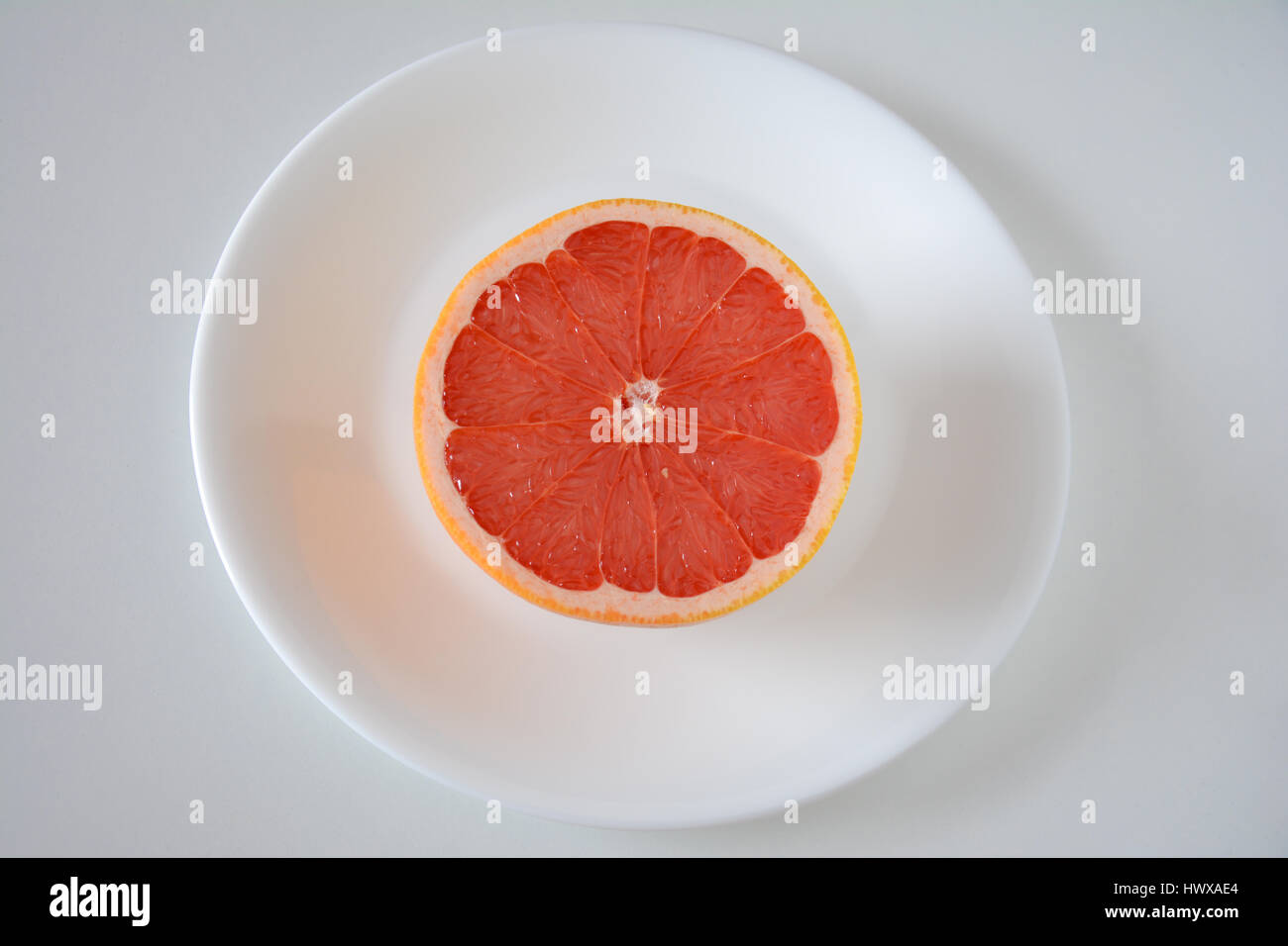 Pompelmo rosa per metà su una piastra bianca e sfondo Foto Stock