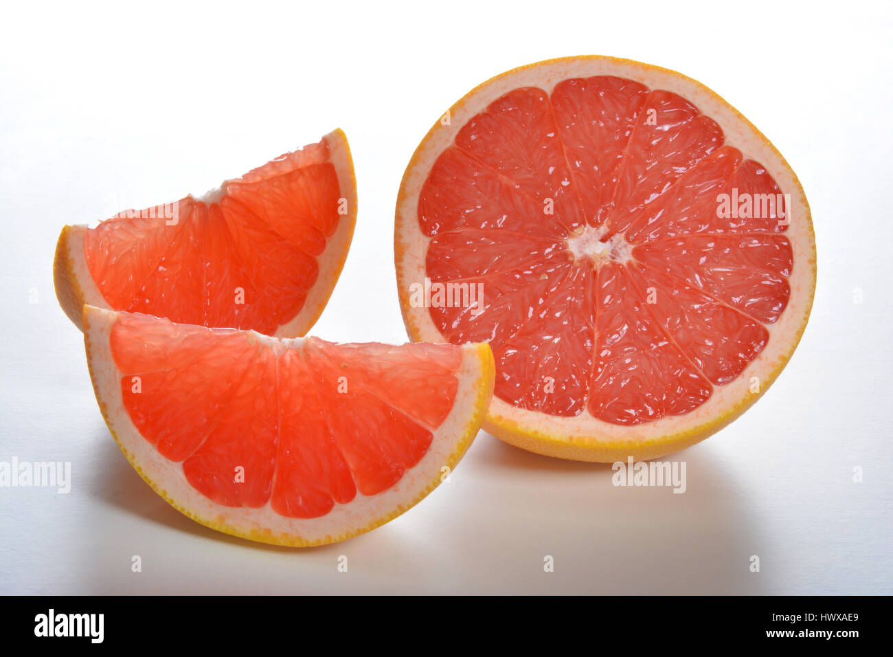 Pompelmo rosa fette e metà su una lavagna bianca Foto Stock