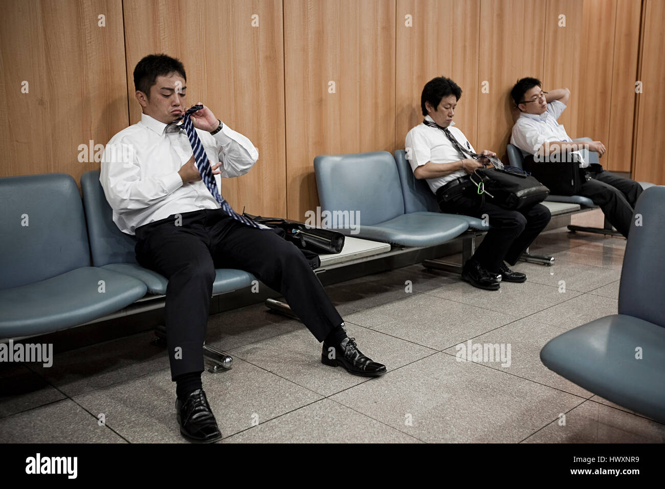 Gli uomini d'affari in attesa per il treno e utilizzando il tempo di legare un tirante, Giappone. Foto Stock