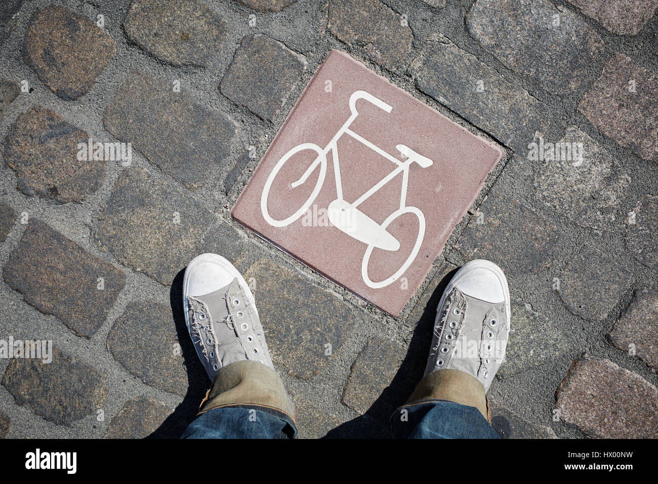 Persona in piedi accanto al pittogramma con bicicletta su cobblestone pavement Foto Stock