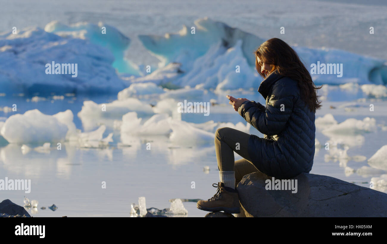 Vista di Profilo di donna che usa il cellulare in remoto di paesaggio vicino congelati ghiacciai in oceano ancora Foto Stock