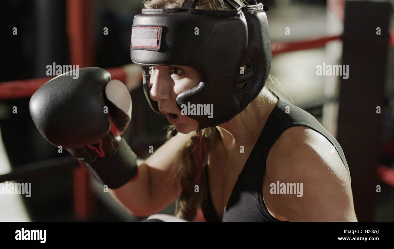 Chiusura del boxer femmina in guantoni da pugilato e casco in piedi di pugilato ring durante il match Foto Stock