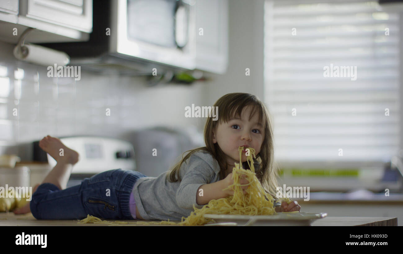 Naughty confuso ragazza posa sul banco di cucina mangiare piatto di spaghetti Foto Stock