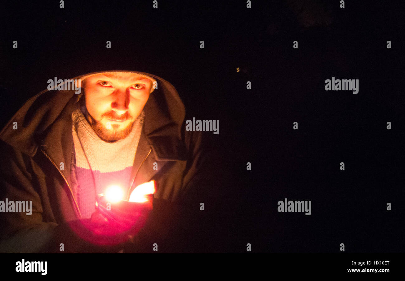 Giovane con un fiammifero che brucia nel buio. Guardando nella telecamera. Foto Stock