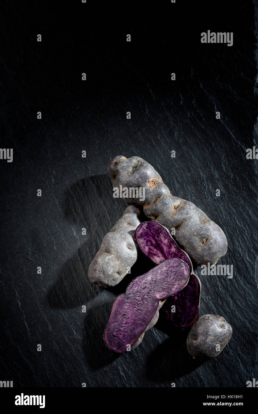 Intero e fette di patate viola sull'ardesia Foto Stock