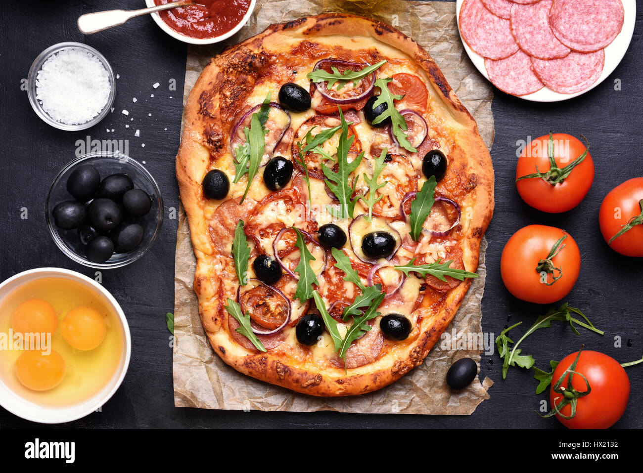 Pizza con pomodoro, salumi e olive su sfondo nero, vista dall'alto Foto Stock