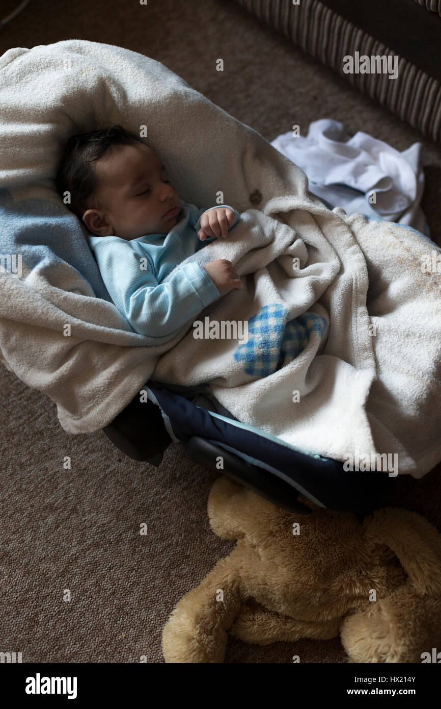 Carino, baby boy è profondamente addormentato nel suo sedile auto. Egli è avvolto in un soffice coperta con un orsacchiotto accanto a lui. Foto Stock