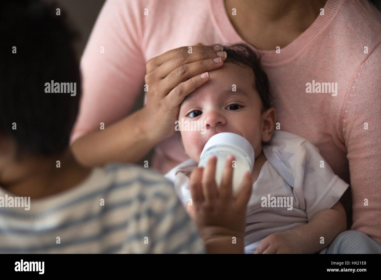 Immagine ravvicinata di un bambino essendo alimentati con una bottiglia di latte dal suo fratello più anziano mentre seduto sulla sua madre giro. Foto Stock
