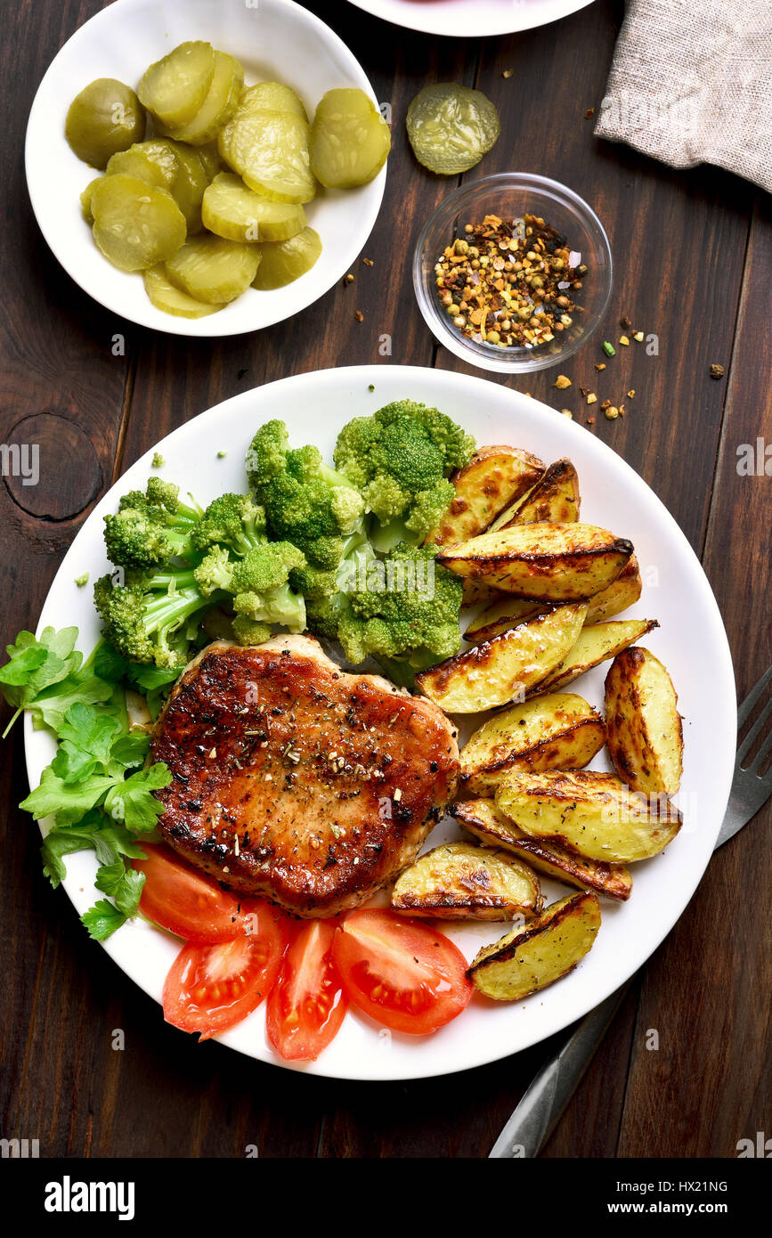 Carne di maiale alla griglia, Spicchi di patate e insalata di verdure, piatto per la cena su sfondo di legno, vista dall'alto Foto Stock