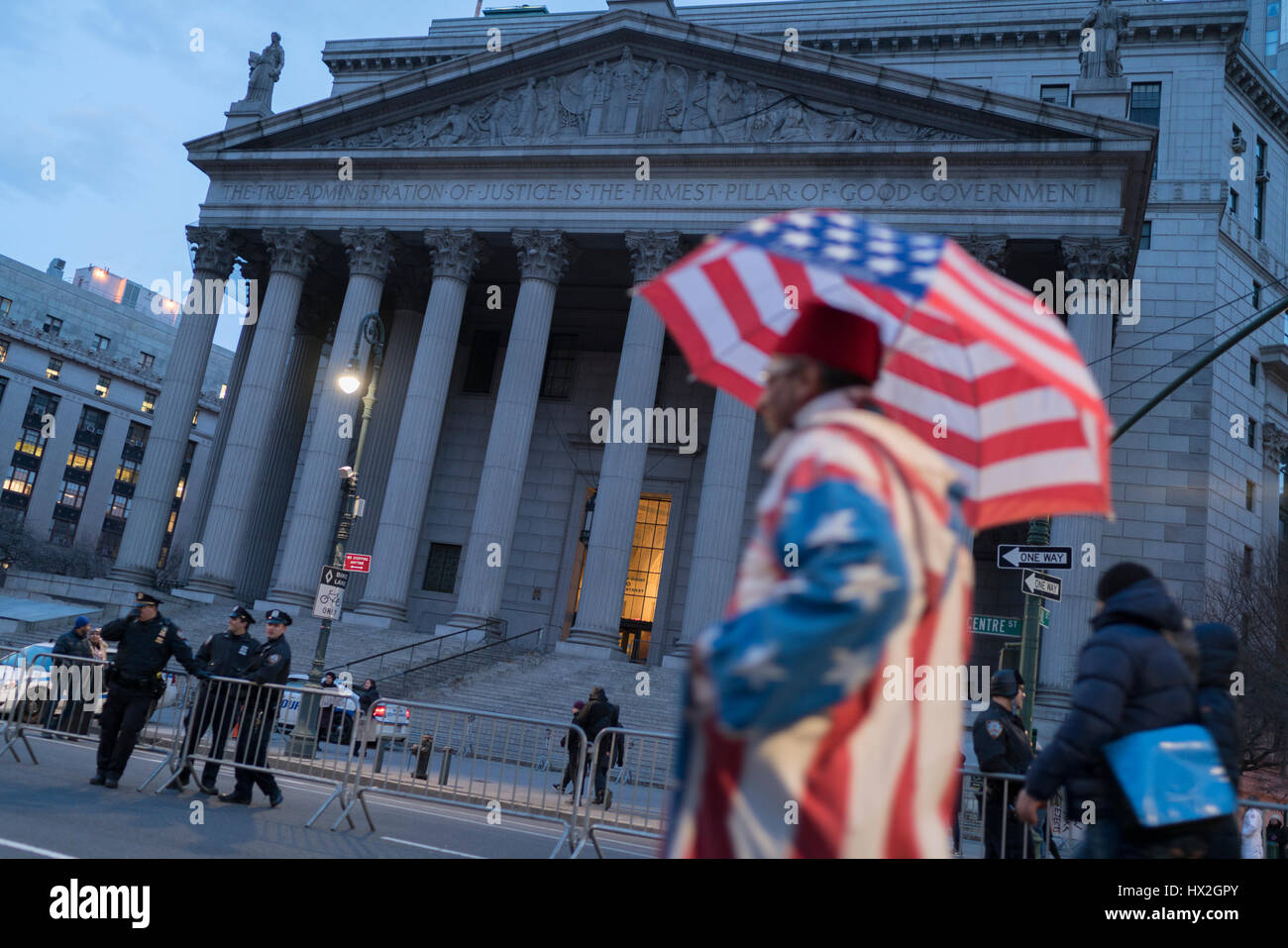 La polizia guarda su dalle fasi di barricate court house. Un manifestante vestita come una bandiera americana che protestavano contro il Presidente Trump's divieto di immigrazione marche dalla. Foto Stock