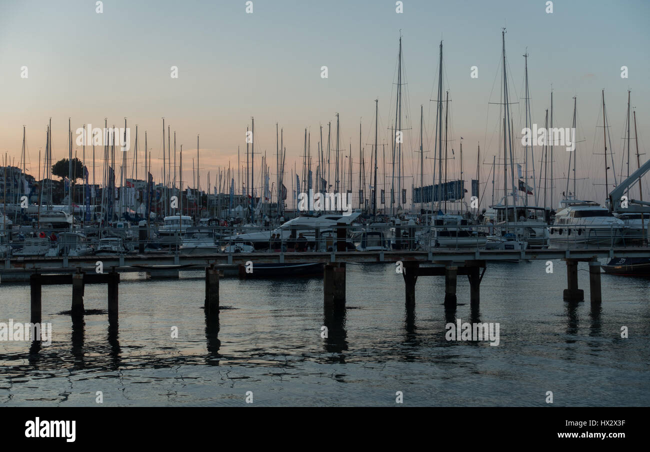 Molti alberi silhouette contro un tramonto Cowes Harbour Marina su una tranquilla ancora duskwith quay post e acque calme, Cowes Week regata, Cowes Regno Unito Foto Stock