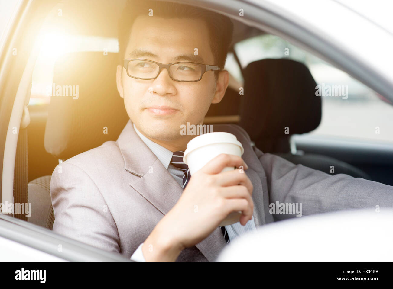 Asian business man di bere il caffè mentre si guida la macchina in una mattina con una bella luce solare. Foto Stock