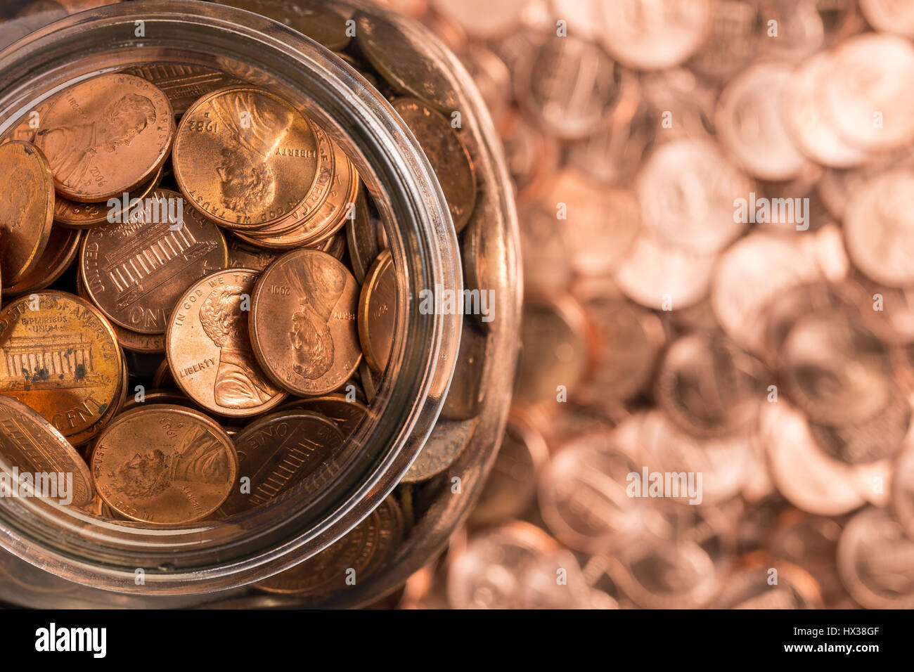 Penny Jar - guardando in giù su un vasetto di spiccioli con più spiccioli come sfondo. Foto Stock