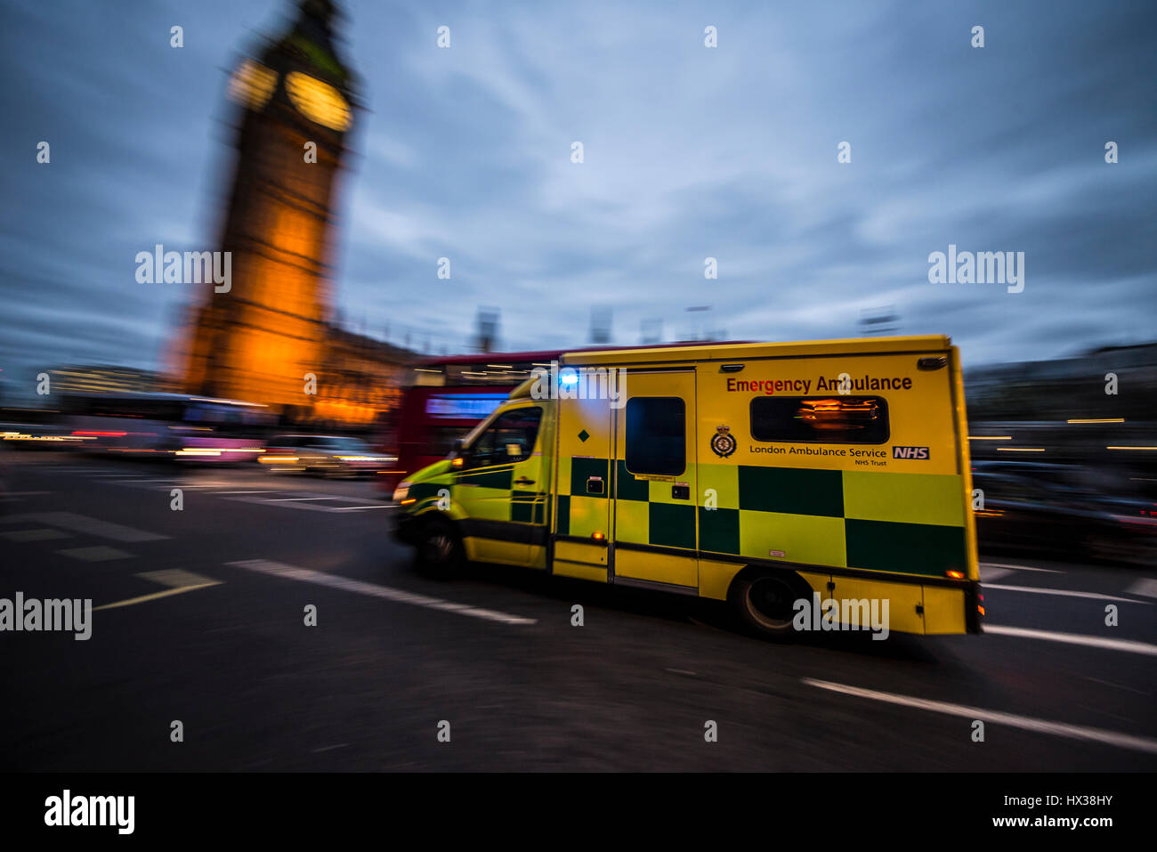 Un ambulanza che viaggiano a velocità al tramonto con luci blu lampeggiante oltre le case del Parlamento a Londra il passaggio di un bus rosso e il big ben Foto Stock