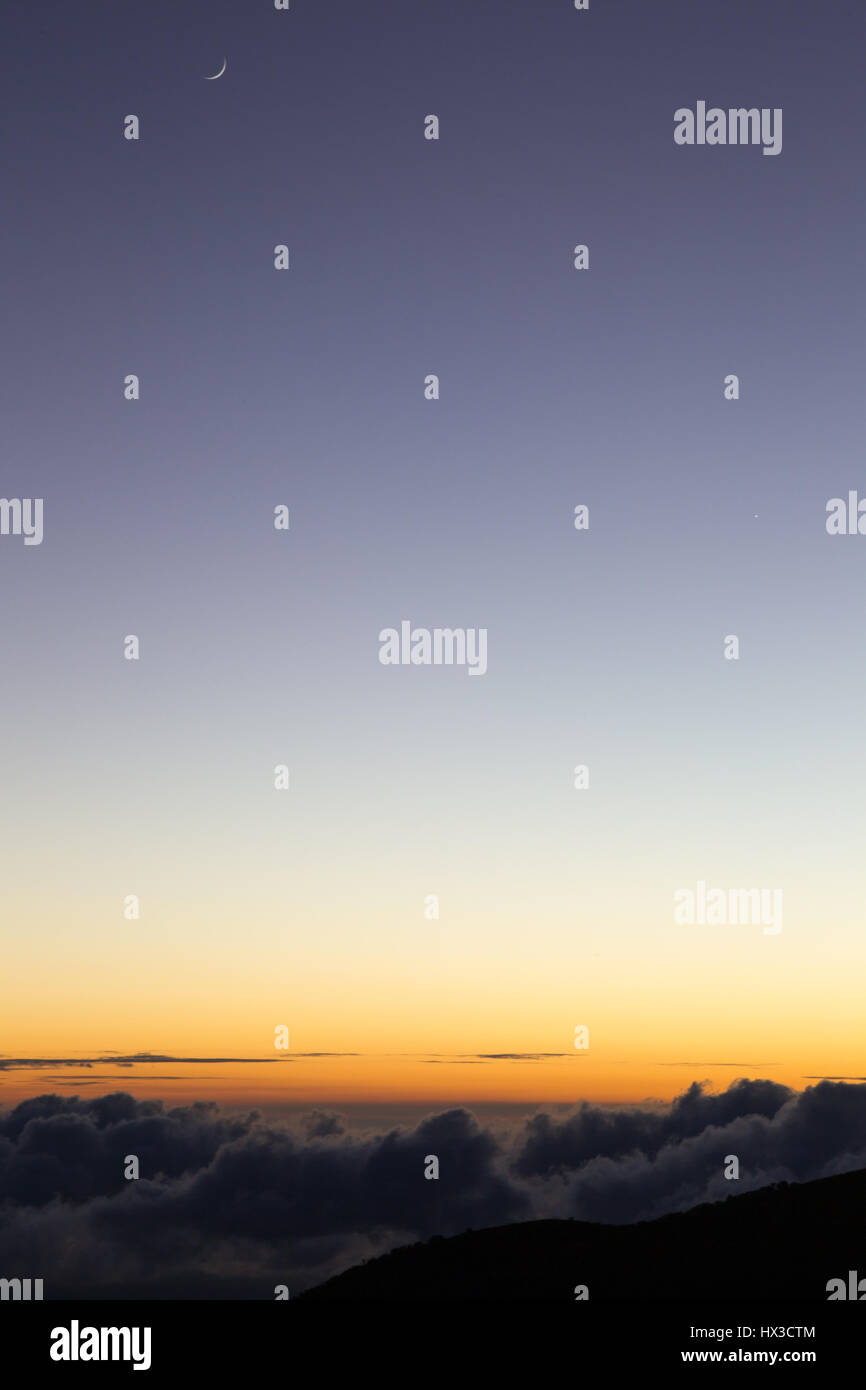 Mezzaluna sopra il luminoso orizzonte arancione accesa dall'ultima luce del tramonto al Mauna Kea sulla Big Island, Hawaii, Stati Uniti d'America. Foto Stock