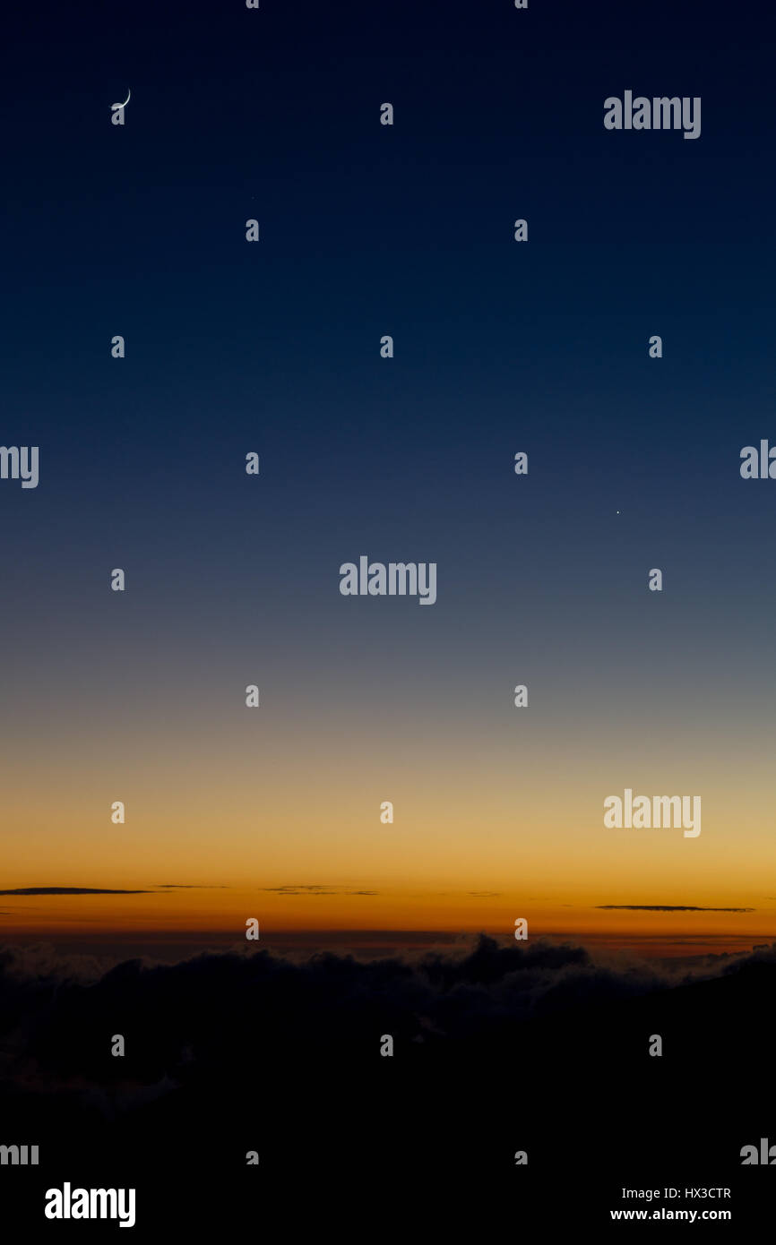 Mezzaluna sopra il luminoso orizzonte arancione accesa dall'ultima luce del tramonto al Mauna Kea sulla Big Island, Hawaii, Stati Uniti d'America. Foto Stock