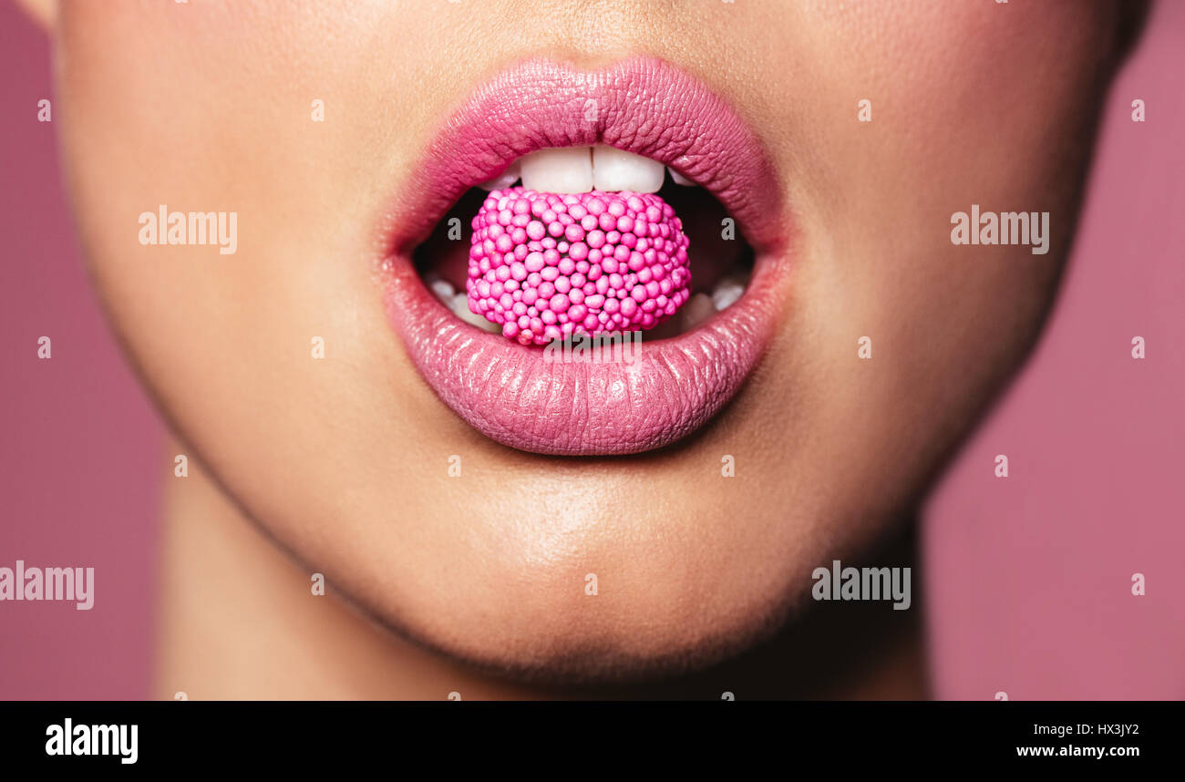 Di un bel colore rosa le labbra con un pezzo di dolce candy. Close up della giovane donna con la caramella in bocca. Foto Stock