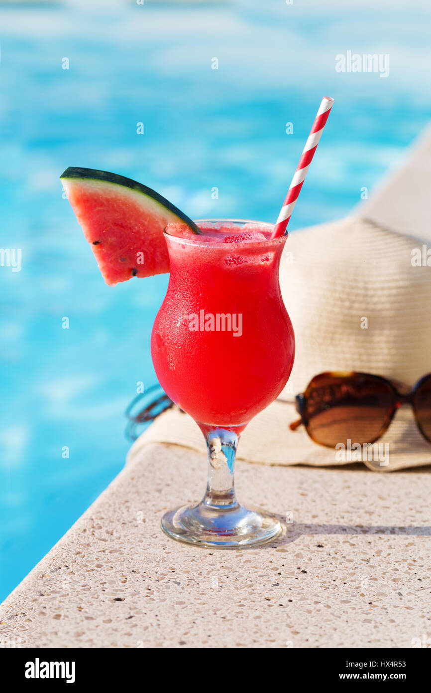 Vetro fresco di acqua-Frullato al melone drink con gli occhiali da sole e cappello di paglia e pantofole sul bordo di una piscina - vacanza concetto tropicale Foto Stock