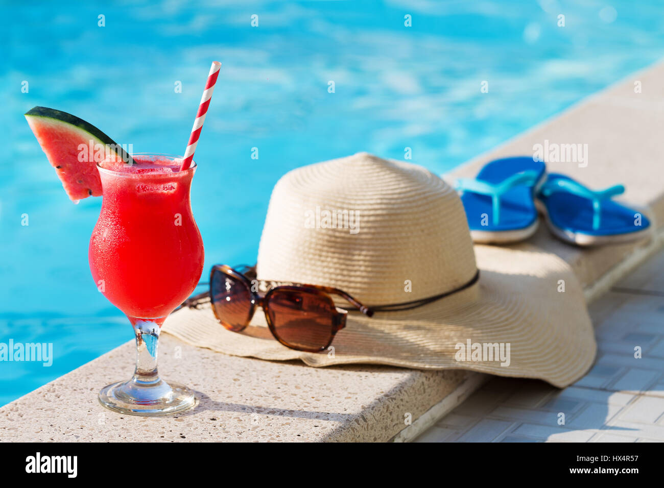 Vetro fresco di acqua-Frullato al melone drink con gli occhiali da sole e cappello di paglia e pantofole sul bordo di una piscina - vacanza concetto tropicale Foto Stock