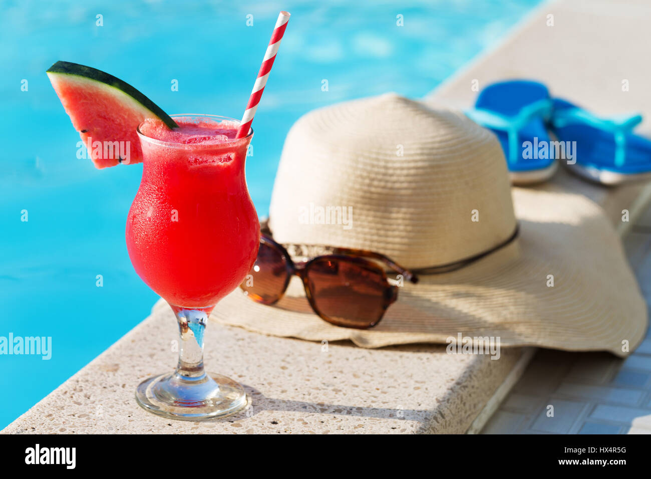 Acqua melone rosso succo fresco drink smoothie cocktail pantofole, cappello di paglia e occhiali da sole vicino alla piscina Foto Stock