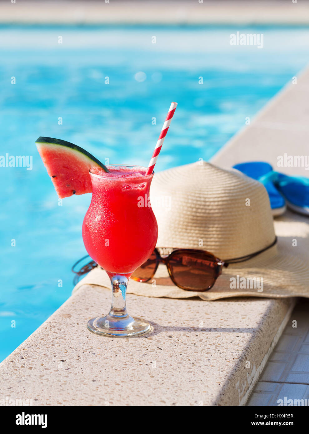 Acqua melone rosso succo fresco drink smoothie cocktail pantofole, cappello di paglia e occhiali da sole vicino alla piscina Foto Stock