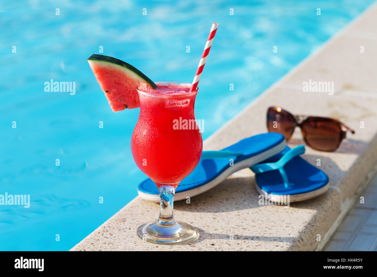 Bicchiere di succo di arancia fresco drink con fiori, occhiali da sole e pantofole sul bordo di una piscina - vacanza concetto tropicale Foto Stock
