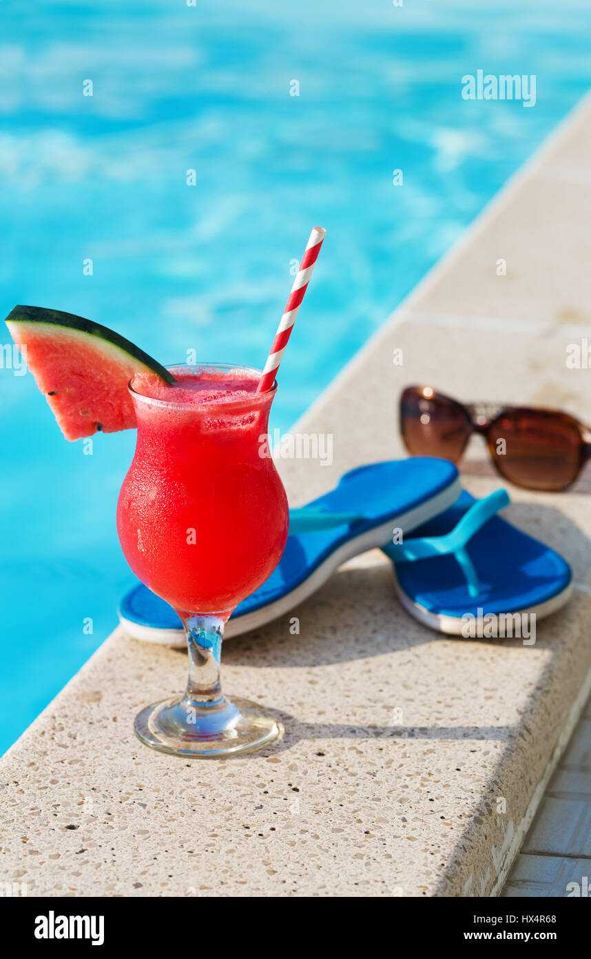 Bicchiere di succo di arancia fresco drink con fiori, occhiali da sole e pantofole sul bordo di una piscina - vacanza concetto tropicale Foto Stock