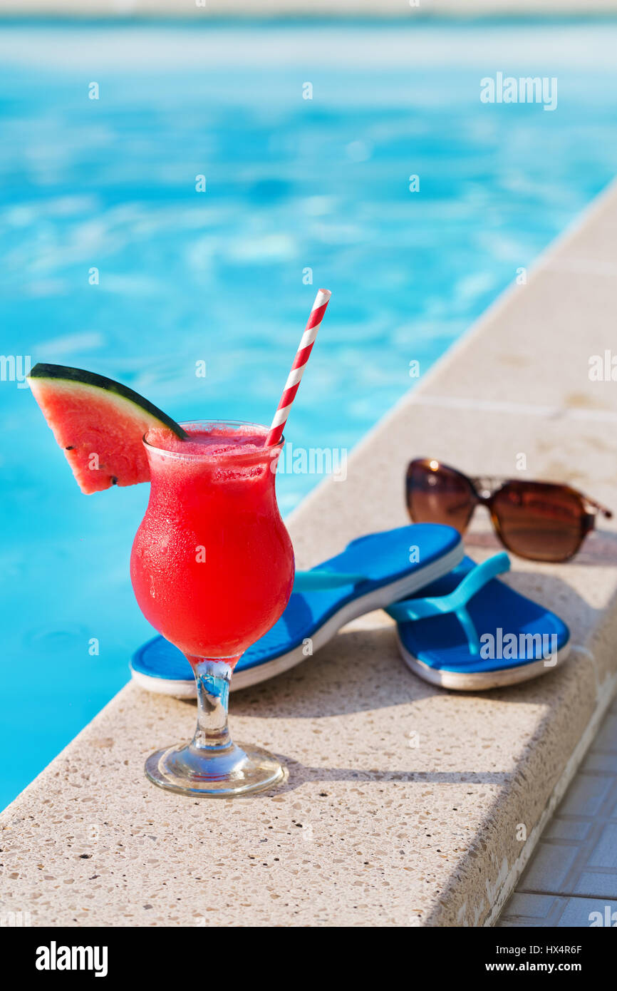 Bicchiere di succo di arancia fresco drink con fiori, occhiali da sole e pantofole sul bordo di una piscina - vacanza concetto tropicale Foto Stock