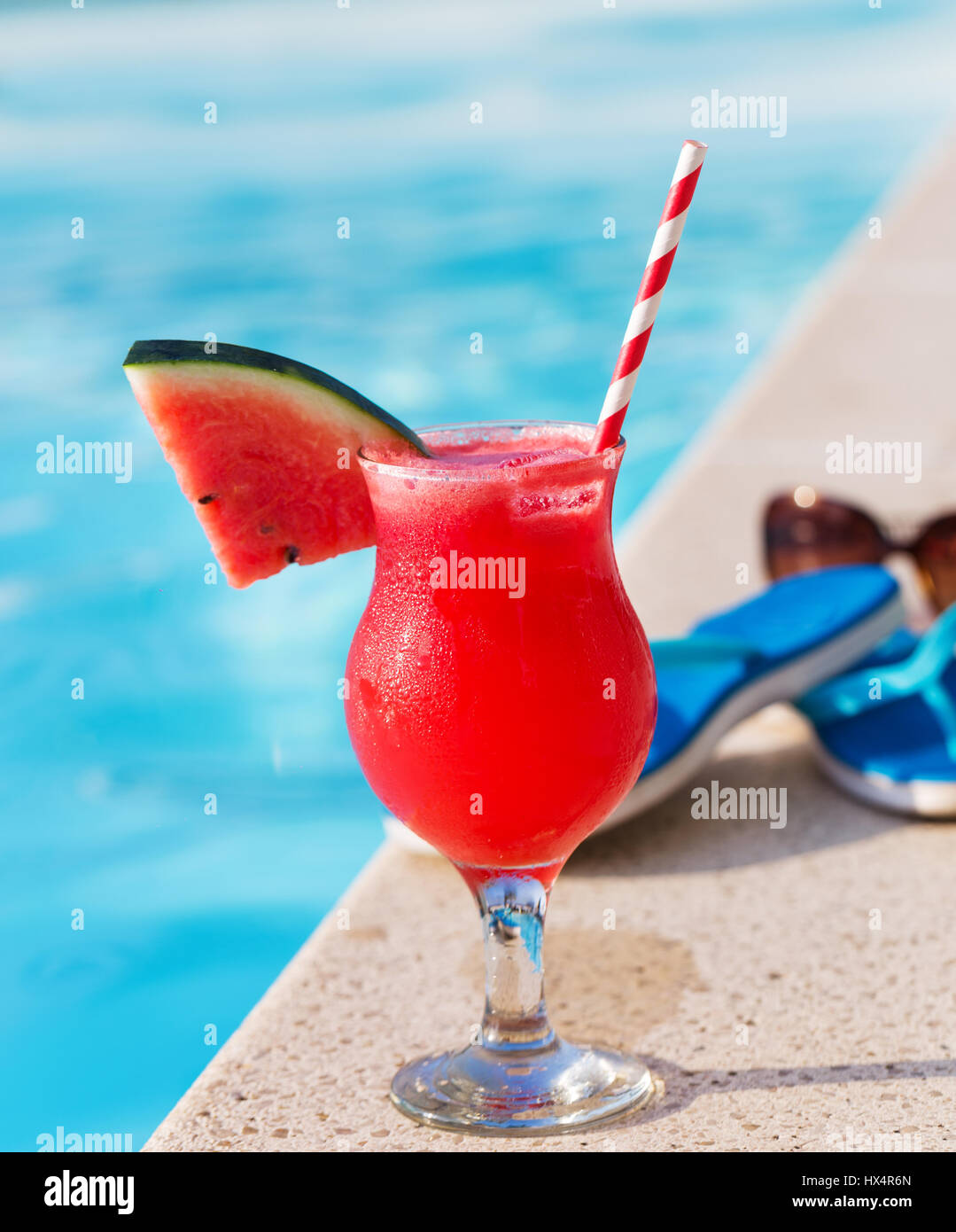 Bicchiere di succo di arancia fresco drink con fiori, occhiali da sole e pantofole sul bordo di una piscina - vacanza concetto tropicale Foto Stock