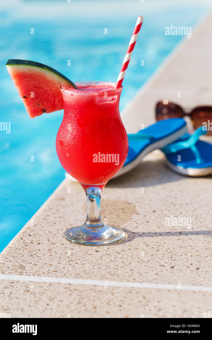Acqua melone rosso succo fresco drink smoothie cocktail pantofole e occhiali da sole vicino alla piscina Foto Stock