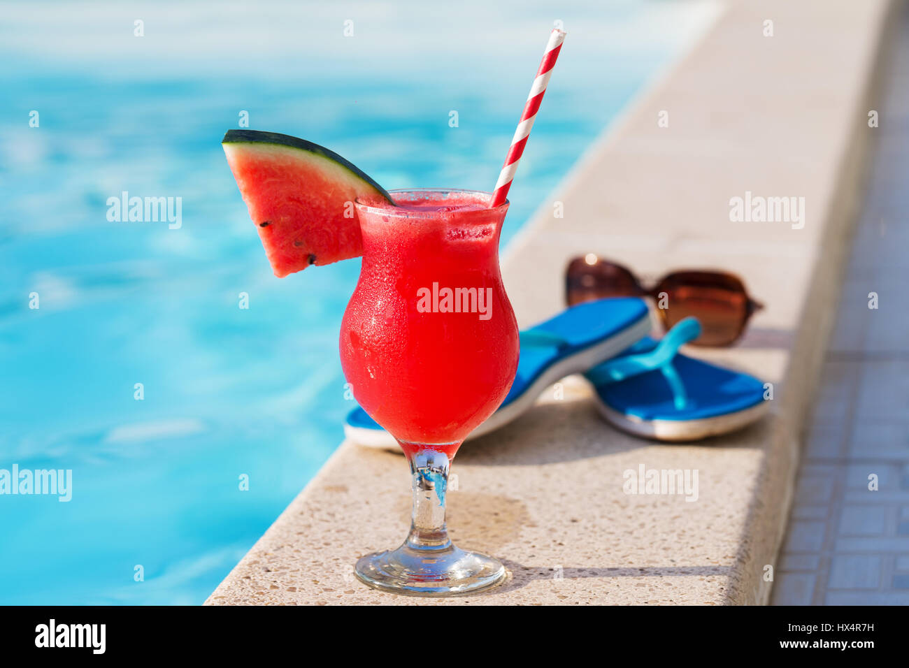 Acqua melone rosso succo fresco drink smoothie cocktail pantofole e occhiali da sole vicino alla piscina Foto Stock