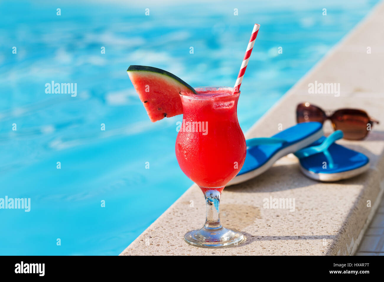Acqua melone rosso succo fresco drink smoothie cocktail pantofole e occhiali da sole vicino alla piscina Foto Stock