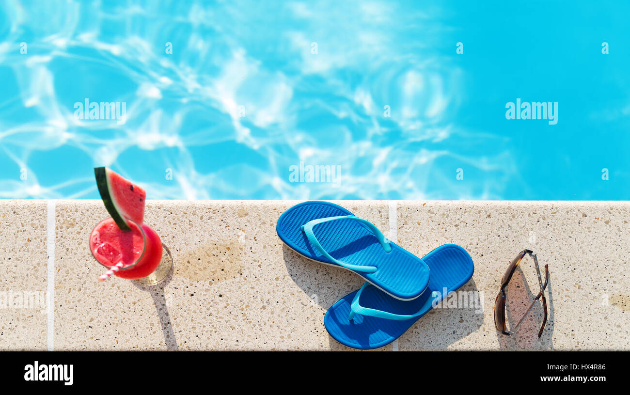 Bicchiere di succo di arancia fresco drink con fiori, occhiali da sole e pantofole sul bordo di una piscina - vacanza concetto tropicale Foto Stock