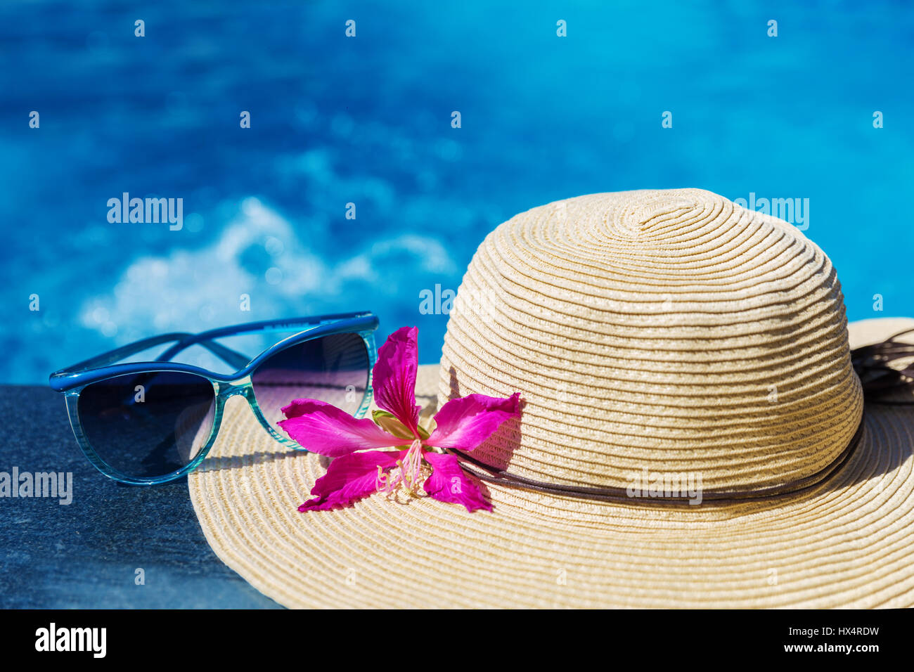 Occhiali da sole con fiore e cappello di paglia sul bordo di una piscina - vacanza concetto tropicale Foto Stock