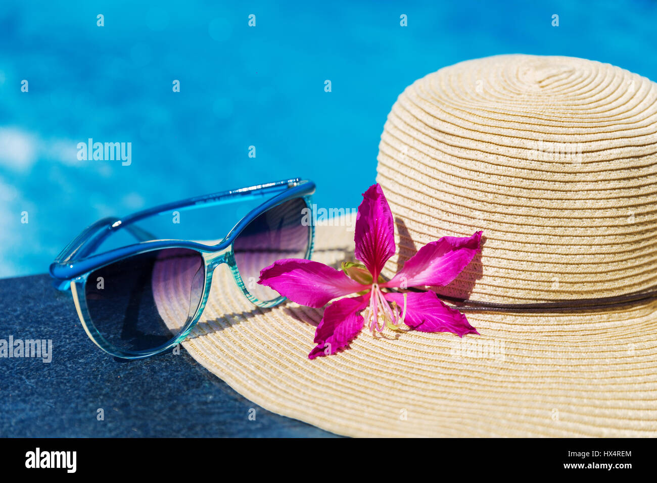 Blue occhiali da sole e cappello di paglia con fiori di orchidea vicino alla piscina - vacanza concept Foto Stock