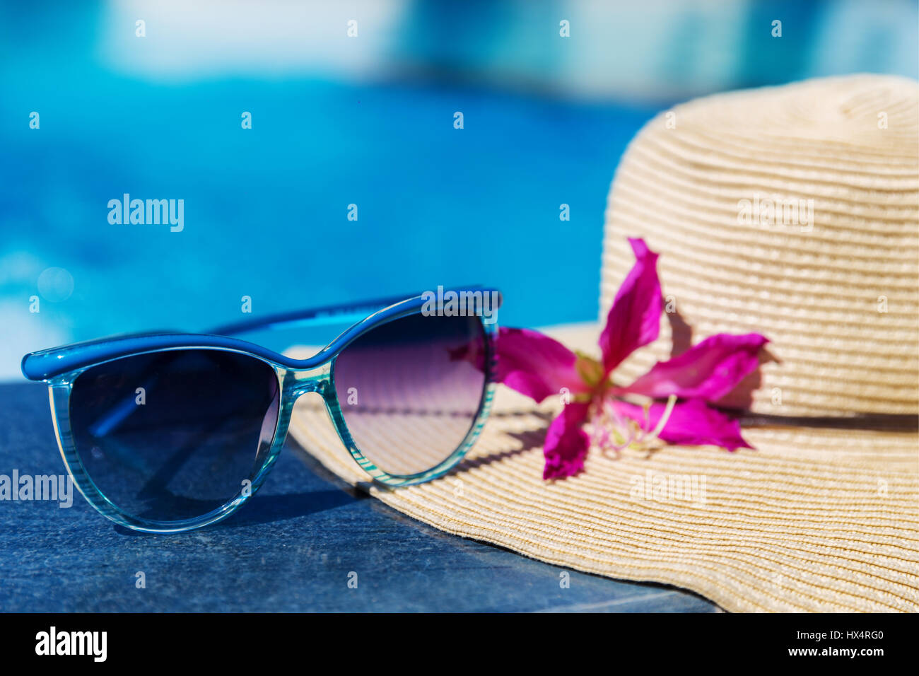 Occhiali da sole con fiore e cappello di paglia sul bordo di una piscina - vacanza concetto tropicale Foto Stock