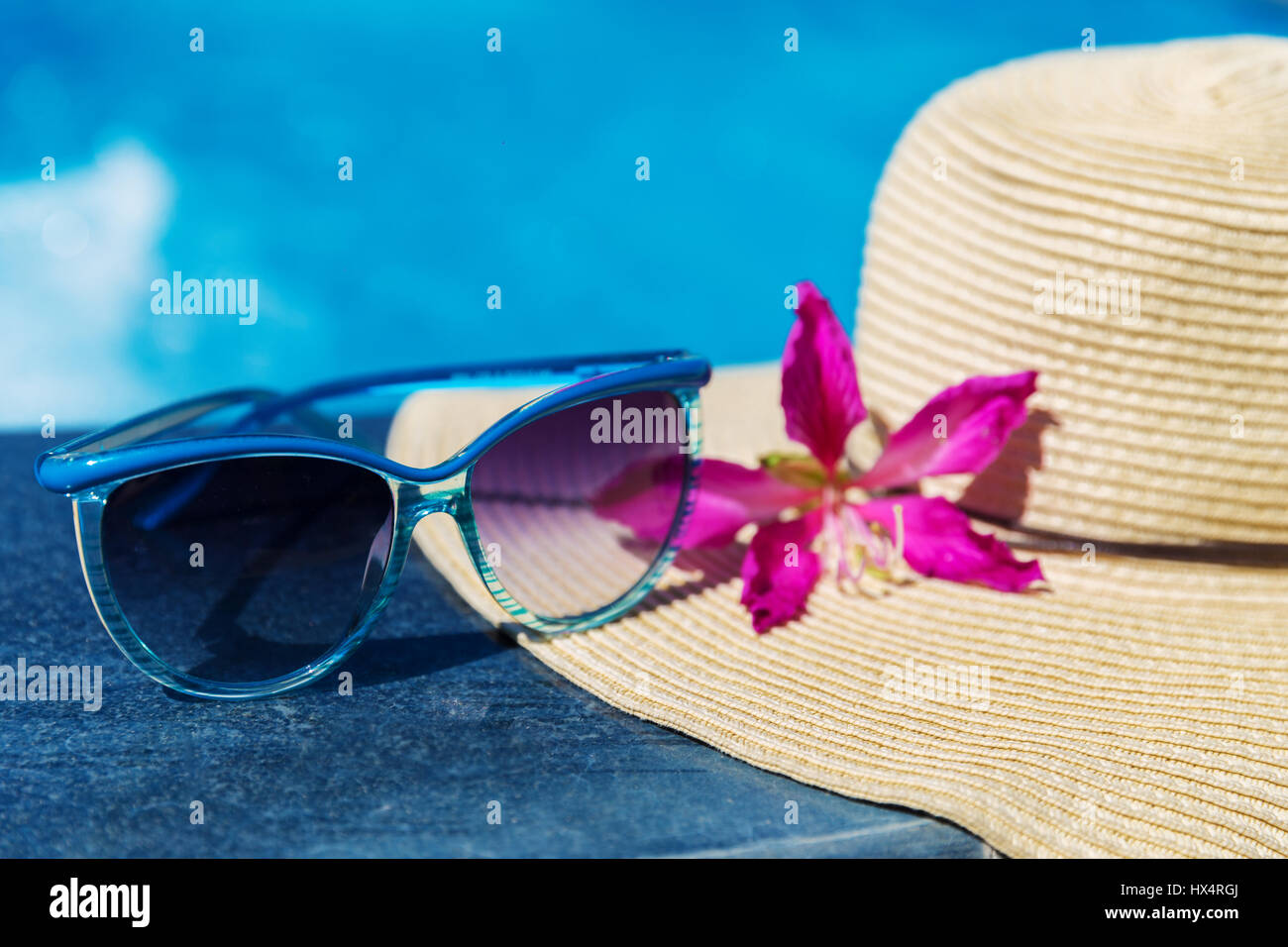 Blue occhiali da sole e cappello di paglia con fiori di orchidea vicino alla piscina - vacanza concept Foto Stock