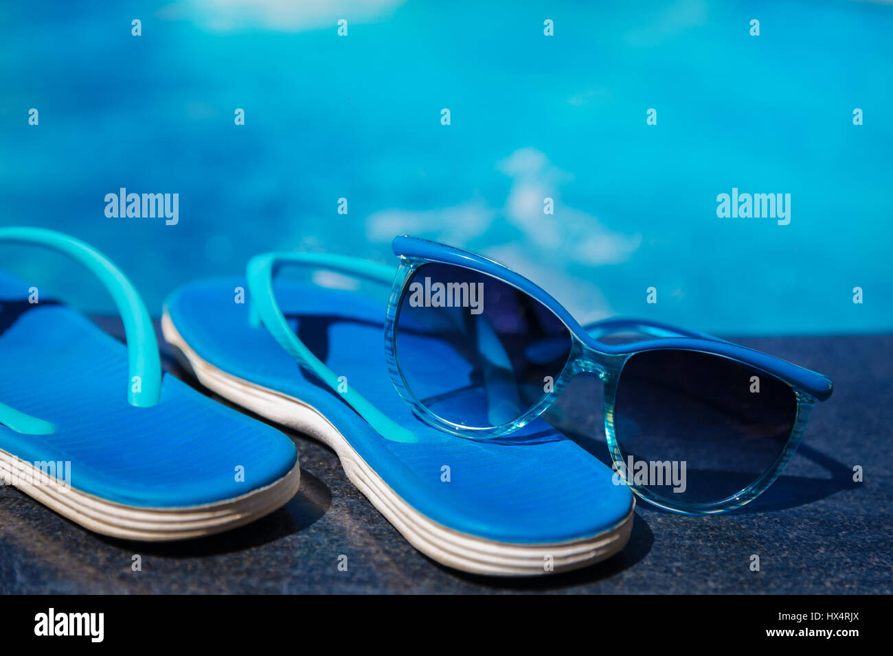 Pantofole blu e occhiali da sole vicino alla piscina - vacanza concept Foto Stock