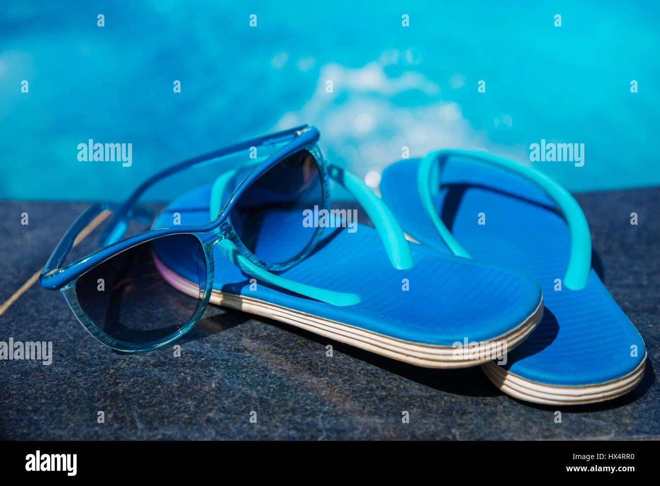 Pantofole blu e gli occhiali da sole sul bordo di una piscina - vacanza concetto tropicale Foto Stock