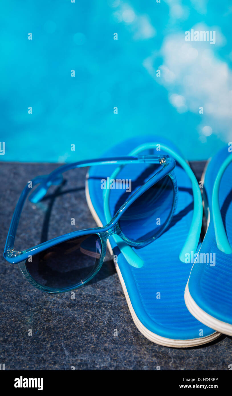 Pantofole blu e occhiali da sole vicino alla piscina - vacanza concept Foto Stock