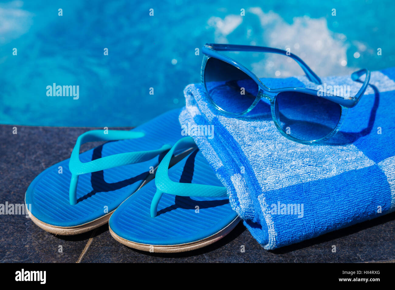 Blue pantofole, occhiali da sole e la salvietta sul bordo di una piscina - vacanza concetto tropicale Foto Stock