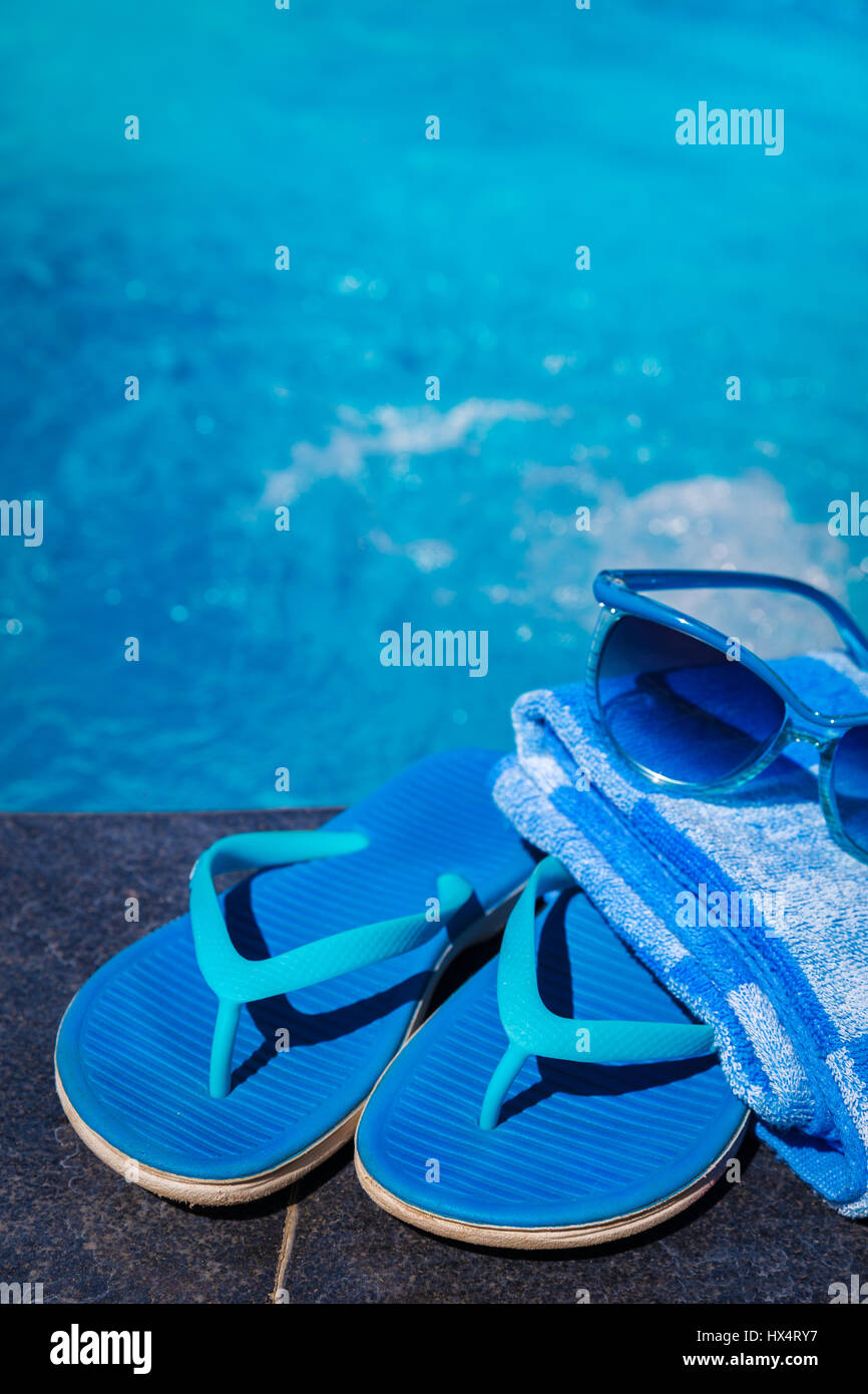 Blue pantofole, occhiali da sole e la salvietta sul bordo di una piscina - vacanza concetto tropicale Foto Stock