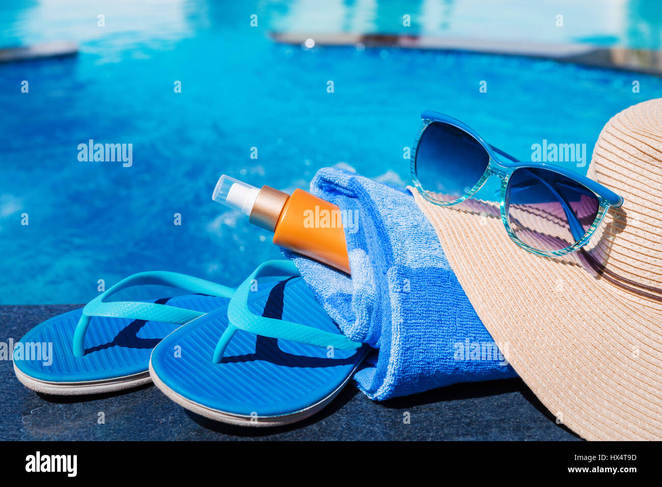 Pantofole blu con crema di protezione solare, asciugamano, cappello di paglia e gli occhiali da sole sul bordo di una piscina - vacanza concetto tropicale Foto Stock